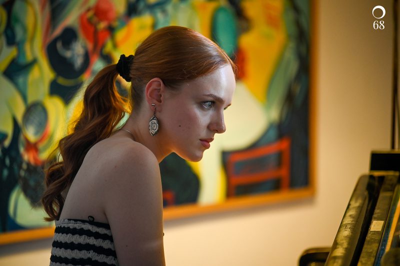 Image of Milda Daunoraite performing at the piano, with a colourful painting on the wall in the background