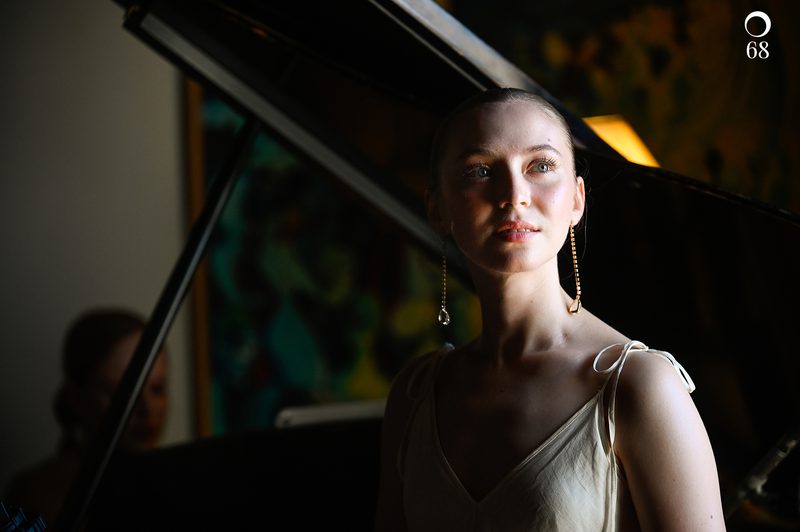 Image of soprano Abigail Sinclair performing, standing in front of a piano looking past the camera