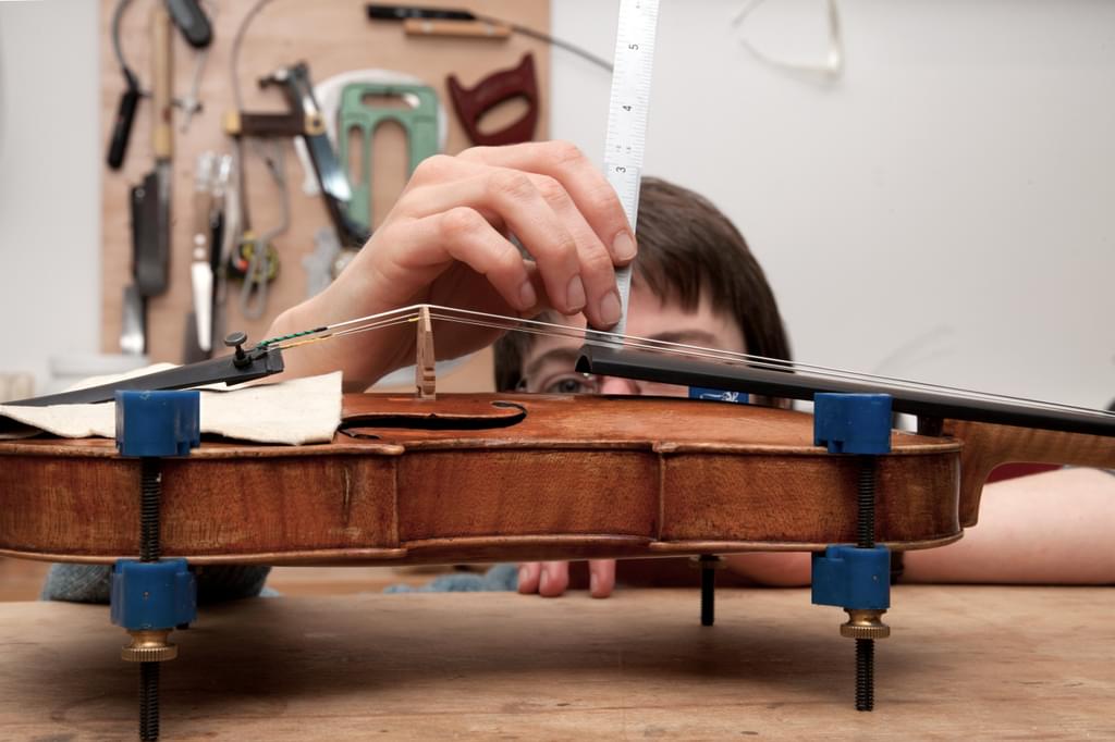 A member of museum staff measures the action on a violin