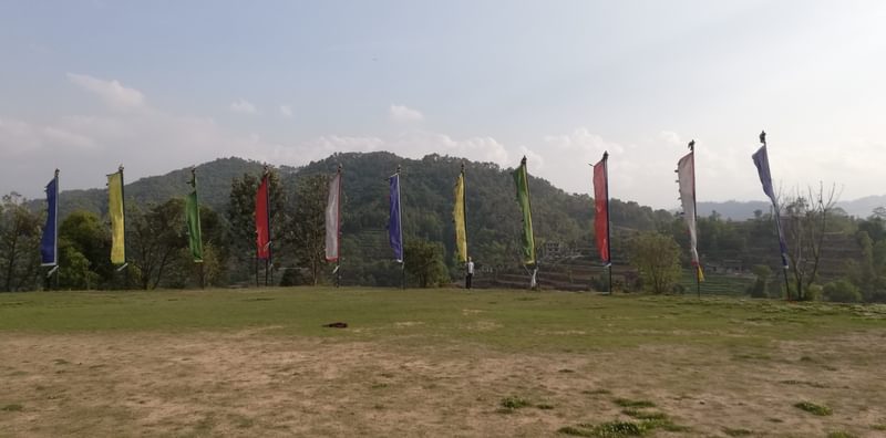 A row of tall coloured flags on a hill in front of a mountain with blue sky and clouds
