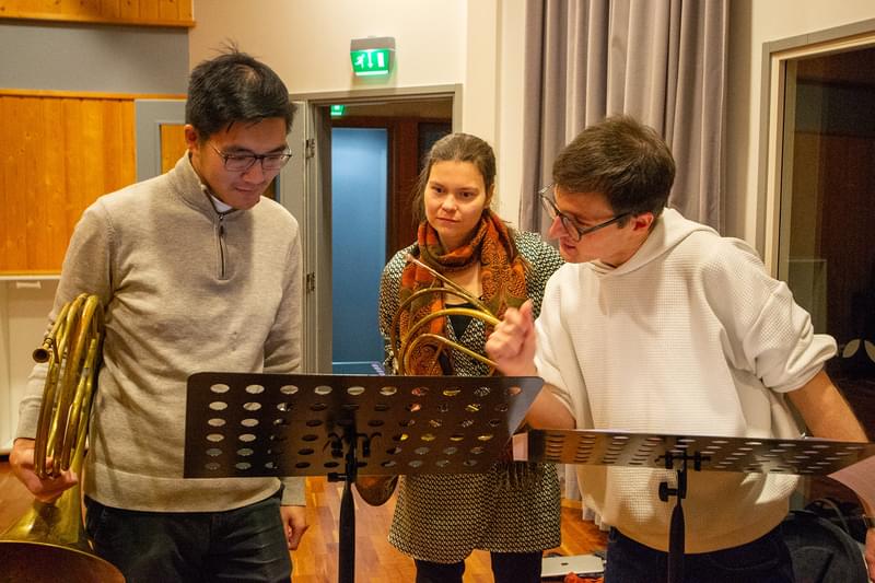 Three music students grouped around a music stand with their instruments