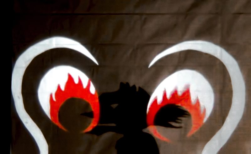 A shadow puppet silhouette overlaid with striking white red and black eyes
