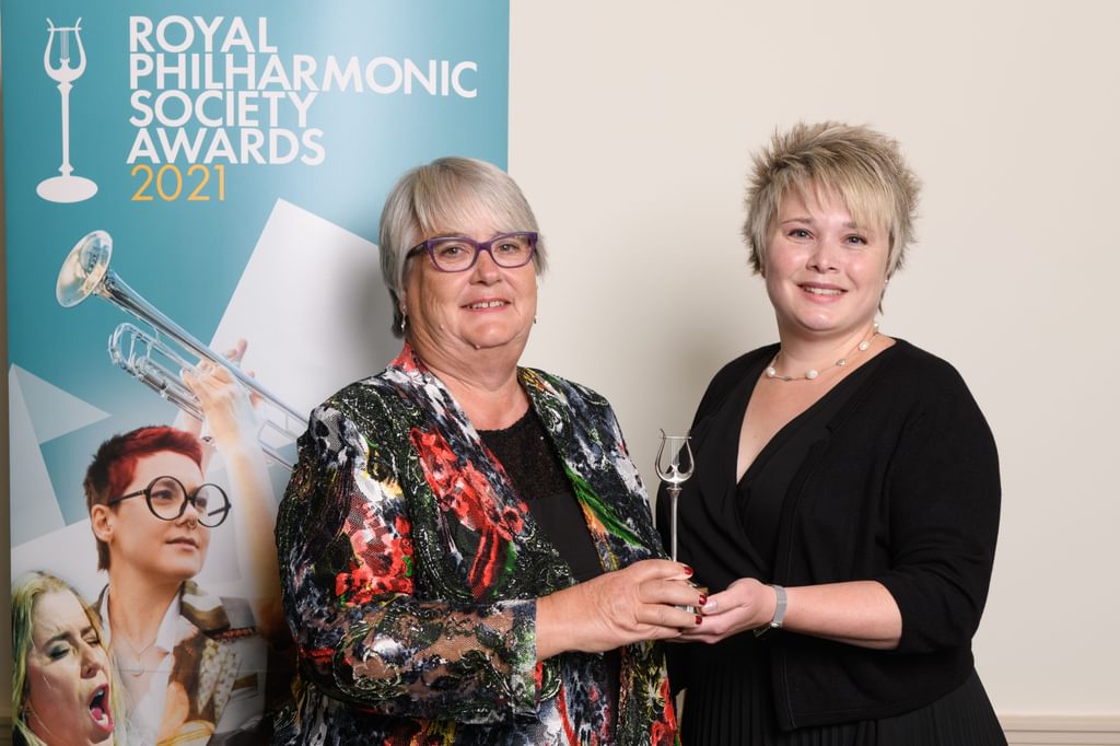 Two people hold an award in hand, smiling to camera