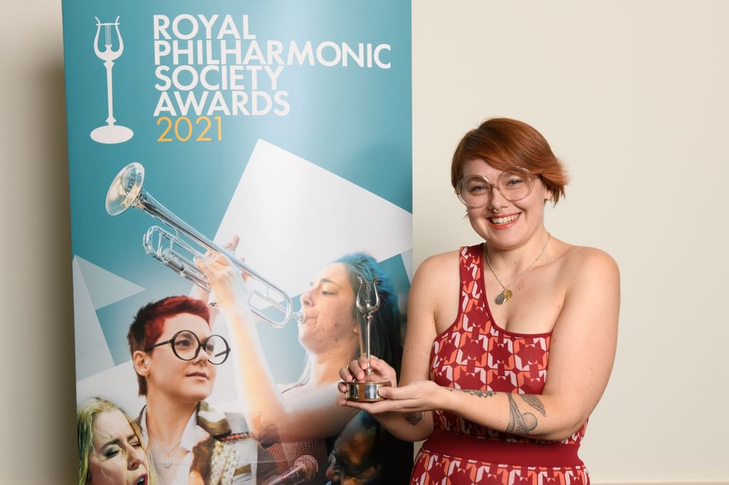 A musician holds an award in hand smiling to camera