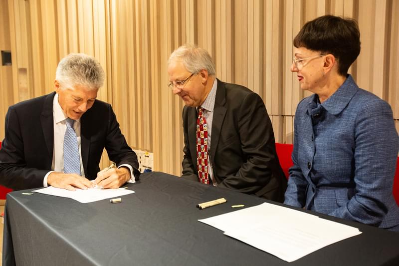 Three people sit at a desk signing documents