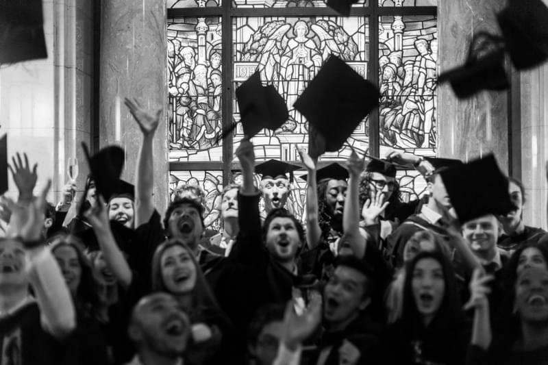Students in graduation gowns throw their mortarboards in the air