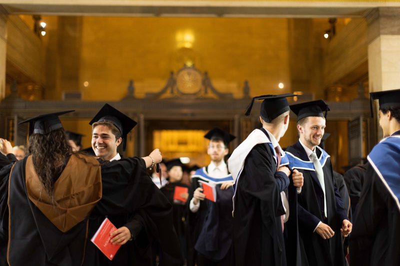 Image of students wearing ceremonial gowns and mortarboards at the 2025 Graduation Ceremony, hugging, smiling and talking