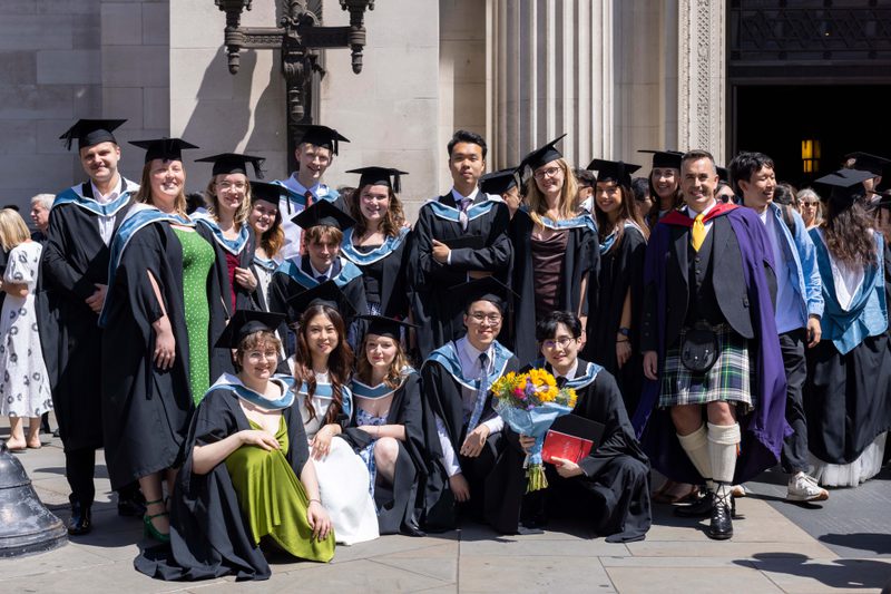 A large group of students posing for a photo, wearing mortarboards and ceremonial gowns, outside Freemason's Hall, London