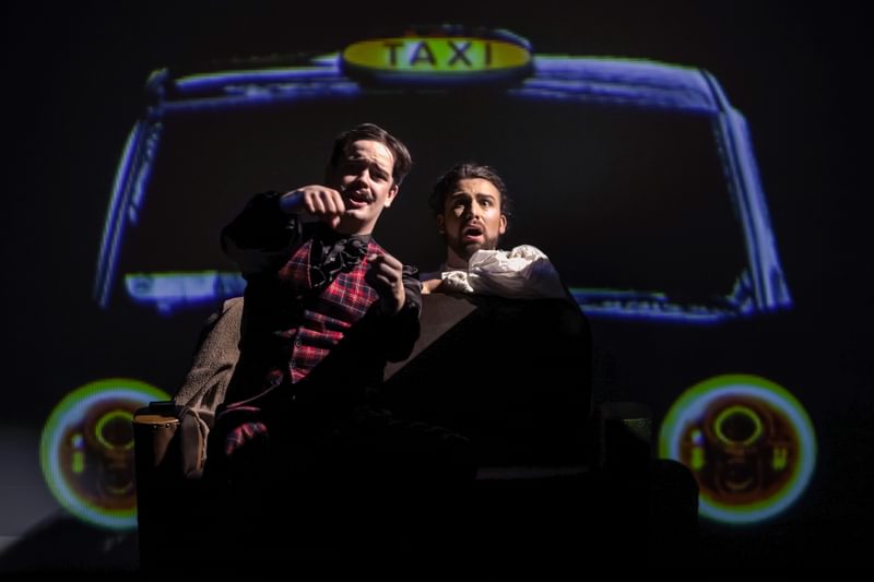 Two opera singers sit on the hood of a taxi