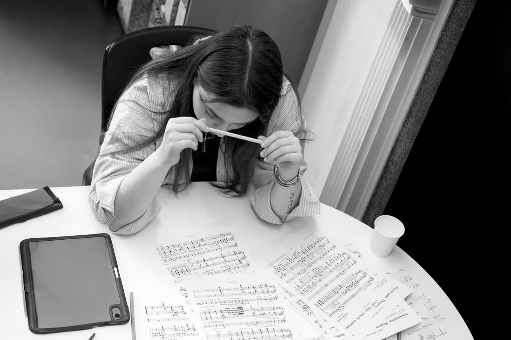 A student sits at a table reviewing sheet music, holding a pencil