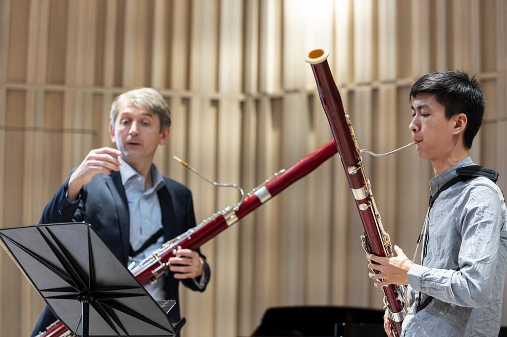 A student plays bassoon to sheet music alongside a teacher