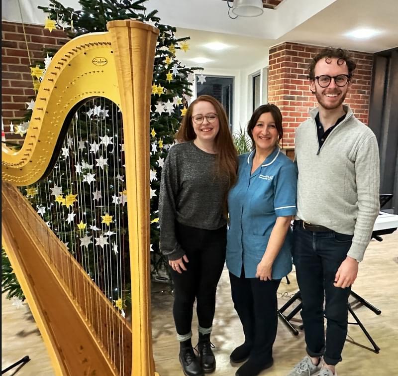 Three musicians stand next to a harp