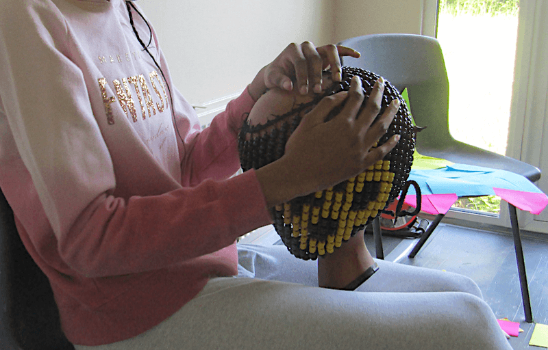 A seated girl playing a beaded percussion instrument