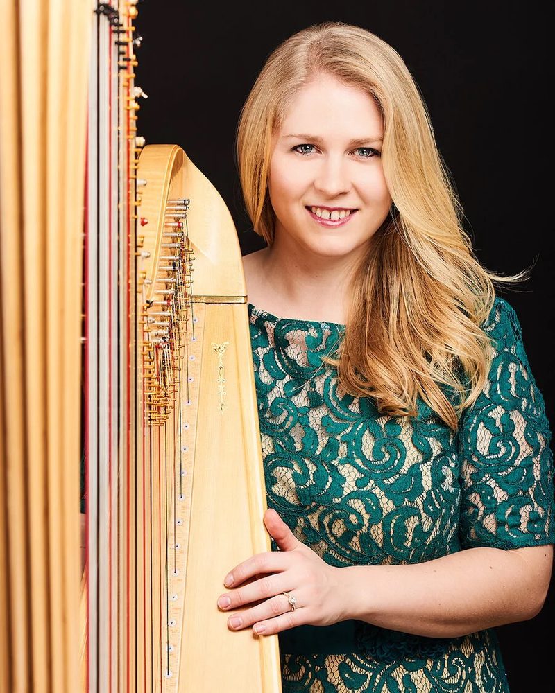 Portrait of Gwenllian Llŷr standing next to a harp, smiling to camera