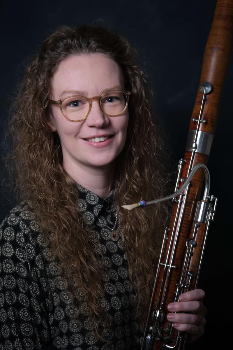 Portrait of Angharad Thomas holding a bassoon, smiling to camera