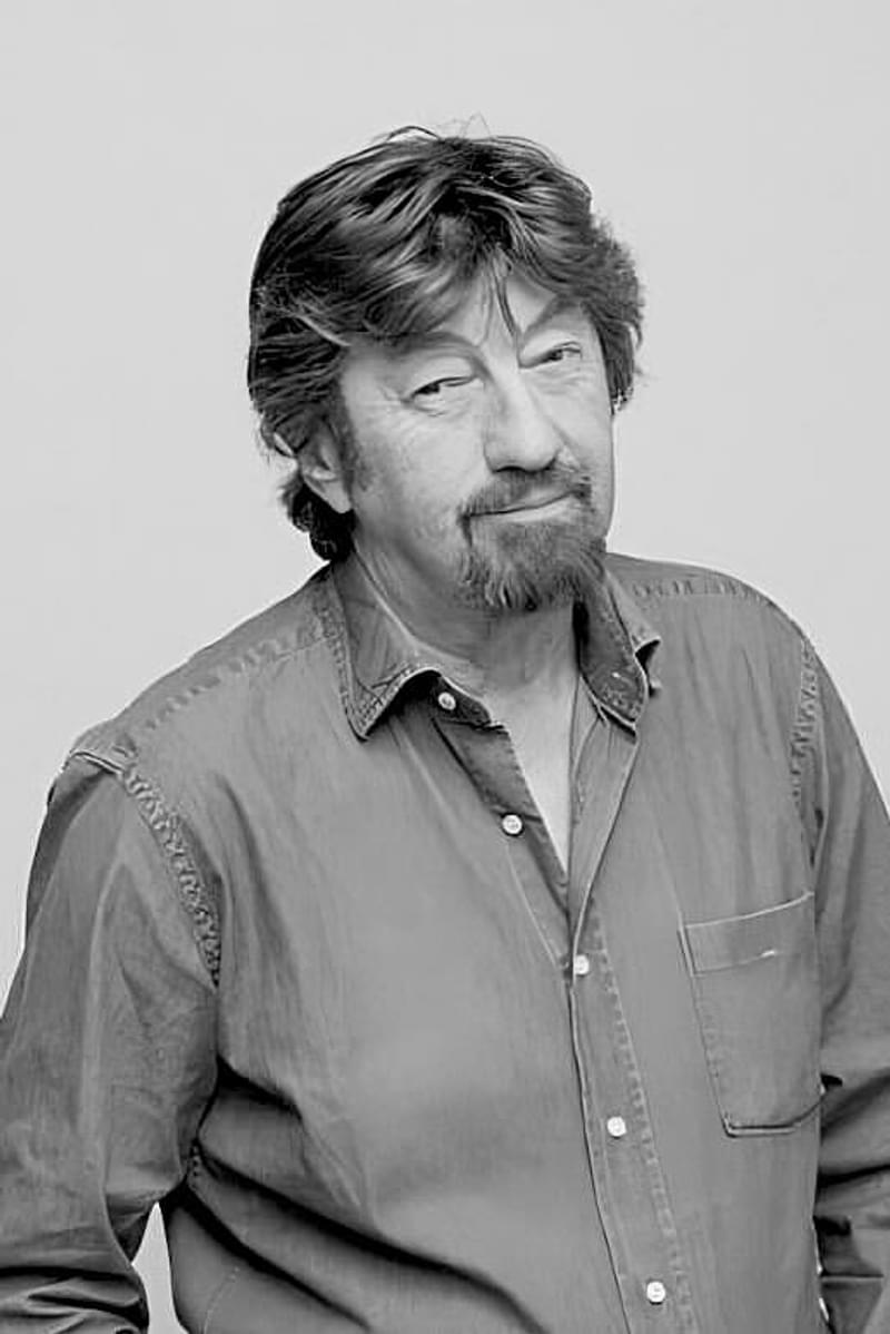 Portrait of Trevor Nunn smiling to camera against cream background (by Joel Redman)