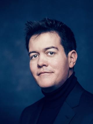 James Baillieu Smiles for headshot against a dark blue background