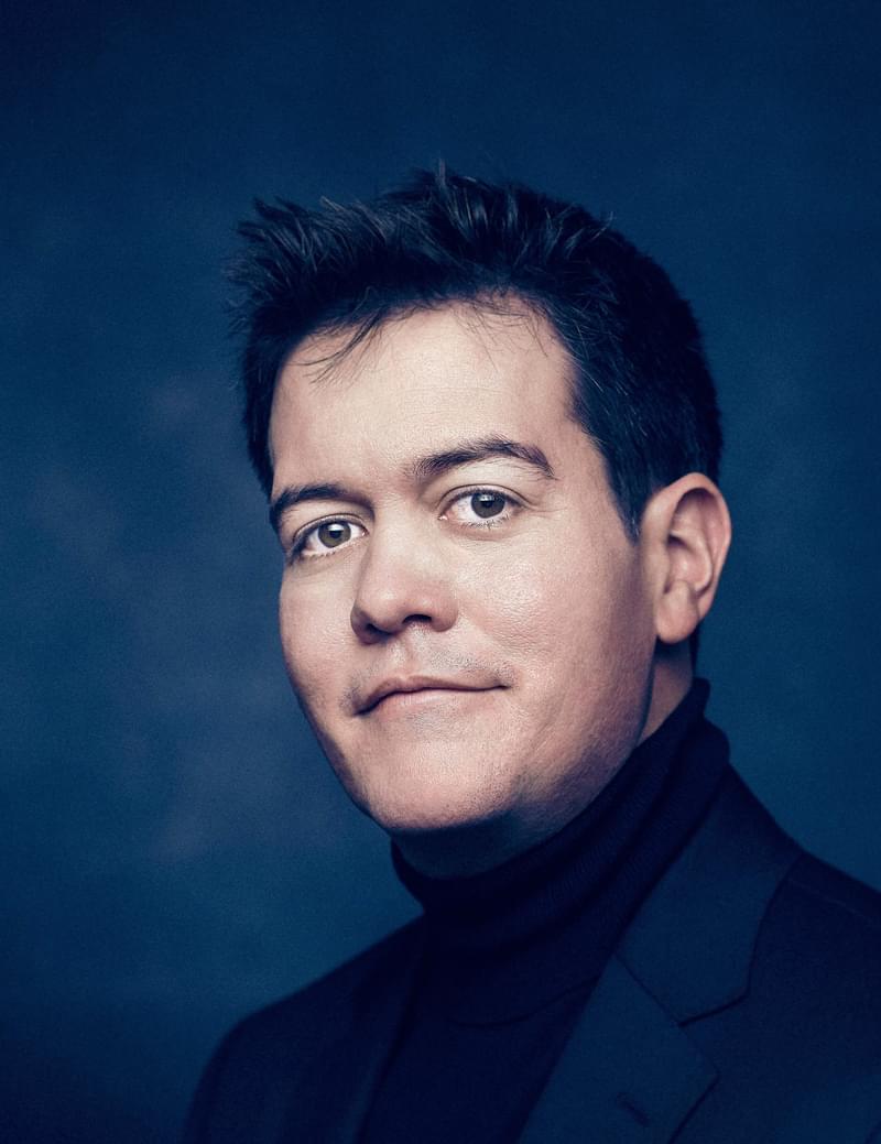 James Baillieu Smiles for headshot against a dark blue background